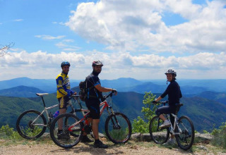 Trois cyclistes avec casques profitent de la vue sur les montagnes au parc de vacances Bivouac nature, Occitanie, France.