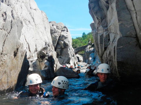 Menschen mit Helmen schwimmen beim Canyoning durch eine Felsenschlucht im Bivouac nature, Occitanie, Frankreich.