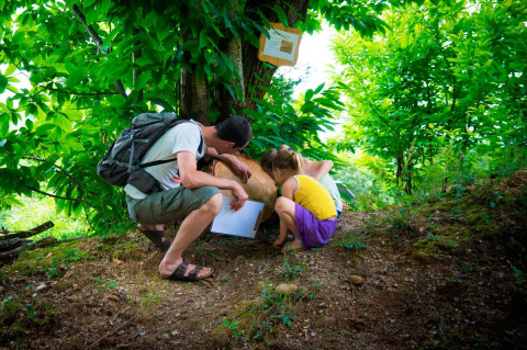En voksen og to børn undersøger naturen i en skov ved Bivouac Nature feriepark i Occitanie, Frankrig.
