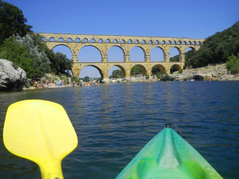 Kajaksejlads på floden nær en historisk stenbro ved Saint Jean du Gard, Occitanie, Frankrig, på en solskinsdag.