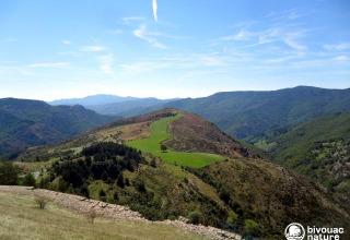 Berglandschaft im Ferienpark Bivouac Nature in Okzitanien, Frankreich, mit grünen Wiesen und blauem Himmel.
