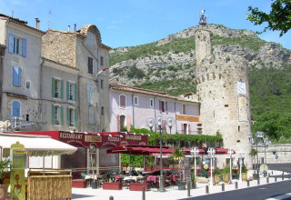Caratteristica strada di Saint Jean du Gard, Occitania, Francia, con caffè, case pastello e torre storica.
