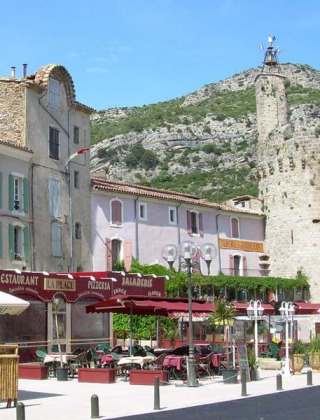 Gezellige straat in Saint Jean du Gard, Occitanie, Frankrijk, met terras, pastelkleurige huizen en toren.