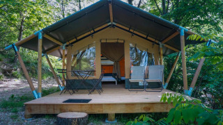 Tente safari Baroudeur avec terrasse en bois, mobilier d'extérieur et cadre verdoyant forestier.