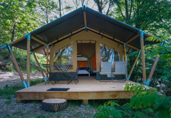 Tenda safari Baroudeur con terrazza in legno, arredi da esterno e ambiente boscoso verde.