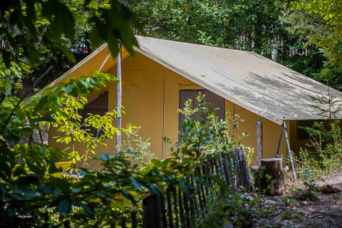 A Canadienne safari tent nestled in lush greenery, surrounded by trees and a rustic wooden fence outdoors.
