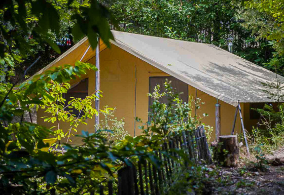 Un safari tent Canadienne entre el follaje verde, rodeado de árboles y una valla de madera rústica.