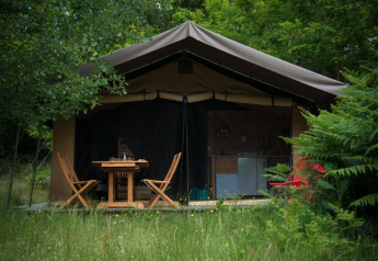 Tenda safari al Bivouac nature in Francia circondata dal verde, con tavolo e sedie in legno davanti.