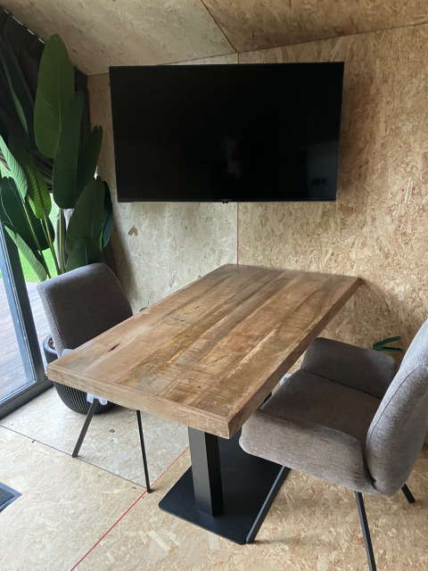 Moderne houten tafel met twee grijze stoelen, zwart tv-scherm en planten bij Solo Retreat, Reestervallei.