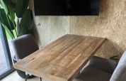 Moderner Holztisch mit zwei grauen Stühlen, schwarzem Fernseher und Pflanzen im Solo Retreat Reestervallei.