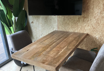 Mesa de madera moderna con dos sillas grises, televisor negro y plantas en Solo Retreat, Reestervallei.