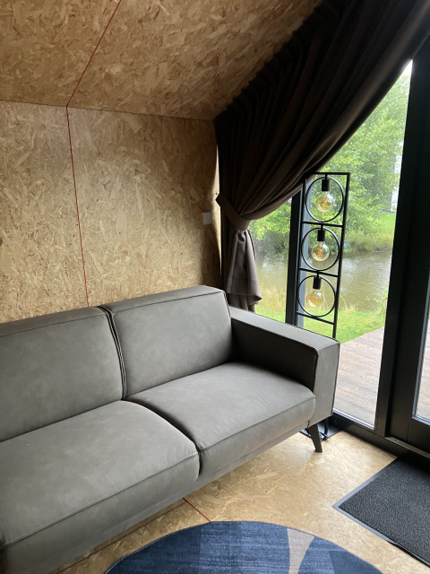 Moderne grijze bank in een stijlvolle lodge met houten wanden, Solo Retreat op Reestervallei, Nederland.