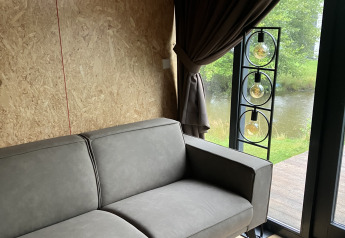Sofá gris moderno en una lodge de madera con vista al exterior, Solo Retreat en Reestervallei, Países Bajos.