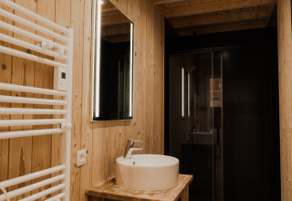 Moderne badkamer met houten wanden, verlicht spiegel en ronde wastafel in Eco Lodge MOBIWOOD, België.