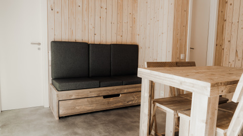 Minimalistisch interieur van Eco Lodge MOBIWOOD met houten meubels en donkere kussens bij Camping Floreal La Roche-en-Ardenne.