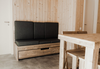 Minimalistisch interieur van Eco Lodge MOBIWOOD met houten meubels en donkere kussens bij Camping Floreal La Roche-en-Ardenne.