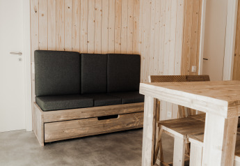 Minimalistisk interiør af Eco Lodge MOBIWOOD med træmøbler og mørke hynder i Camping Floreal La Roche-en-Ardenne.