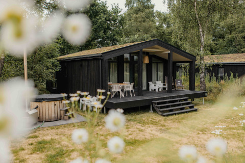 The Hills lodge met hottub bij Wilsumer Berge, Duitsland, omgeven door natuur en wilde bloemen op de voorgrond.