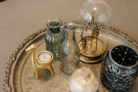 Decoratief dienblad met glazen flessen, gouden dierenkaars, insecten onder stolp en keramiek.