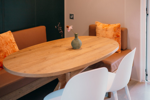 Table en bois avec vase et fleur, banquette marron et chaises blanches aux Tiny Wander Lodges, Pays-Bas.