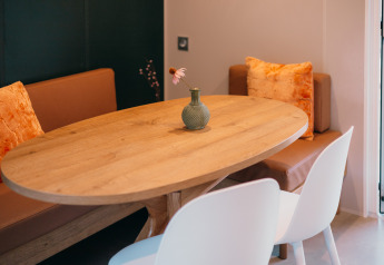 Table en bois avec vase et fleur, banquette marron et chaises blanches aux Tiny Wander Lodges, Pays-Bas.