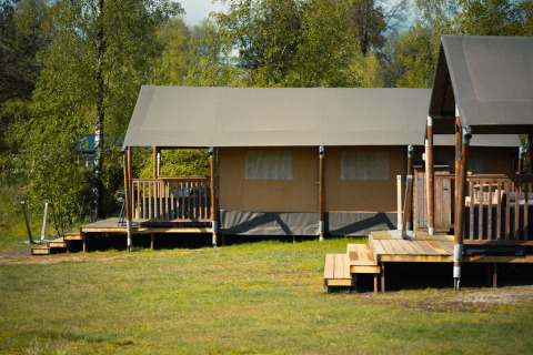 Safari tent at Wilsumer Berge in Germany, surrounded by trees and grassy open space in the foreground.