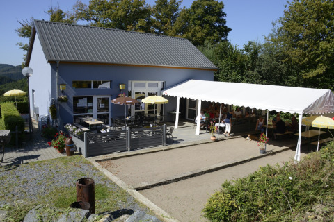 Area caffè all'aperto con ospiti, ombrelloni e tendone al Camping Liefrange a Wiltz, Lussemburgo.