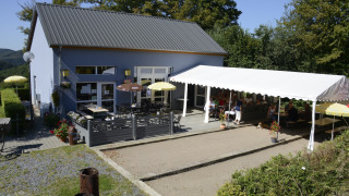 Außencafé mit Gästen, Sonnenschirmen und Zeltüberdachung im Camping Liefrange in Wiltz, Luxemburg.