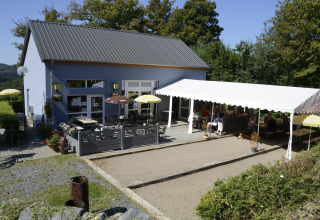 Terrasse de café avec clients, parasols et auvent au Camping Liefrange à Wiltz, Luxembourg.