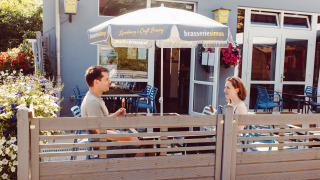 Zwei Personen genießen Eis unter einem Sonnenschirm auf Camping Liefrange in Wiltz, Luxemburg.