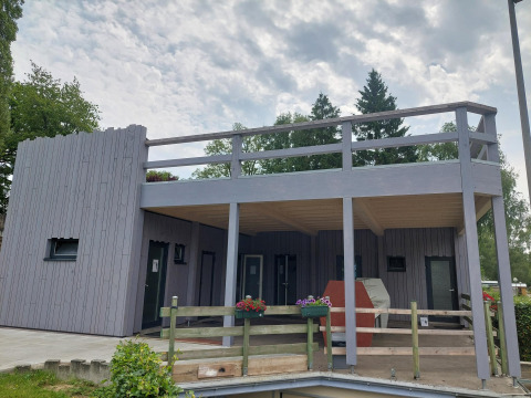 Modern holiday cabin with wooden terrace at Camping Liefrange, Wiltz, Luxembourg under a cloudy sky.