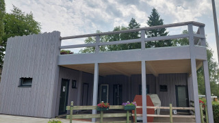 Modernes Ferienhaus mit Holzterrasse im Camping Liefrange in Wiltz, Luxemburg unter bewölktem Himmel.