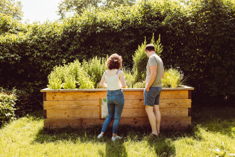 Two people stand by a raised garden bed in the sunny yard at Camping Liefrange, Wiltz, Luxembourg.