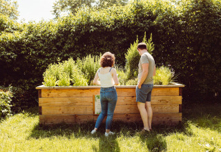 Two people stand by a raised garden bed in the sunny yard at Camping Liefrange, Wiltz, Luxembourg.