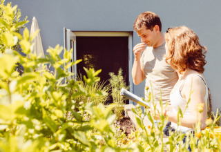 Two people enjoy the garden at their holiday home at Camping Liefrange in Wiltz, Luxembourg, surrounded by plants.