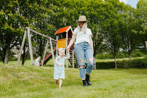 Madre e hijo juegan en césped junto a un parque infantil en Camping Liefrange, Wiltz, Luxemburgo.