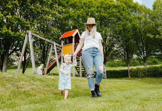Madre e bambino giocano sull’erba vicino a un parco giochi a Camping Liefrange, Wiltz, Lussemburgo.