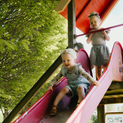 Zwei kleine Kinder spielen auf einer Rutsche im Ferienpark Camping Liefrange in Wiltz, Luxemburg, unter Bäumen.