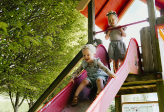 Deux jeunes enfants jouent sur un toboggan sous des arbres verts au Camping Liefrange à Wiltz, Luxembourg.