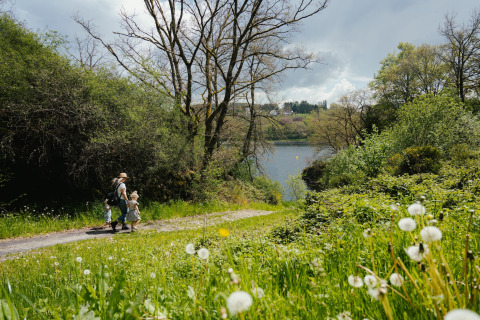 Familie går på sti gennem grønt landskab med udsigt til sø, natur og træer i Camping Liefrange, Wiltz.