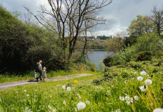 Famille marchant sur un sentier verdoyant près d’un lac à Camping Liefrange, parc de vacances à Wiltz.