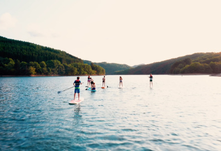 Menschen paddeln auf einem ruhigen See bei Liefrange, Wiltz, Luxemburg, umgeben von grünen Hügeln.
