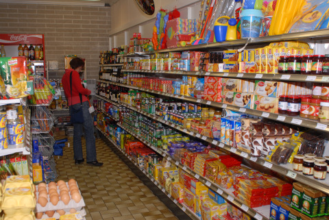 Een persoon winkelt in een glamping supermarkt met goed gevulde schappen vol etenswaren en kruidenierswaren.
