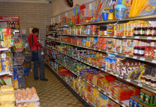 Una persona fa la spesa in un piccolo market di glamping con scaffali pieni di cibo e prodotti vari.