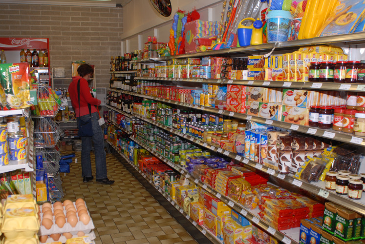 Una persona fa la spesa in un piccolo market di glamping con scaffali pieni di cibo e prodotti vari.