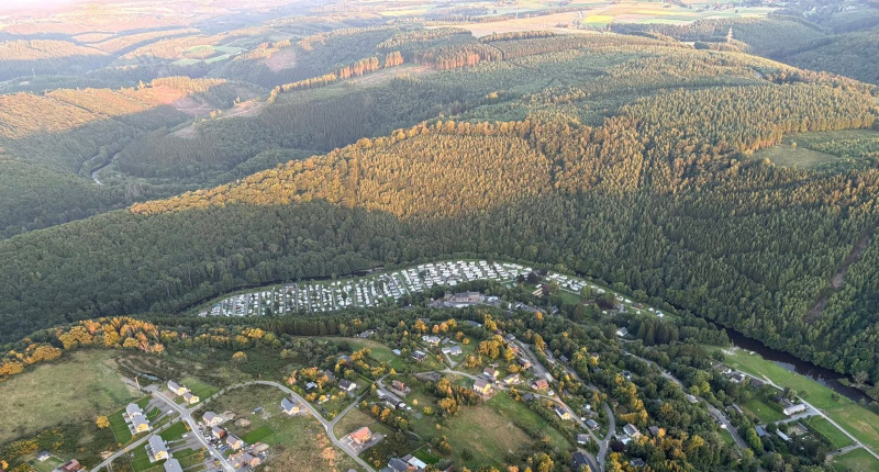 Luchtfoto van een glampinglocatie tussen beboste heuvels, met huizen en campings op de voorgrond.