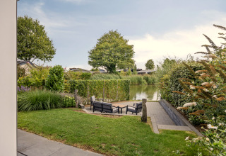 Vue d’un lodge au Recreatiepark het Esmeer aux Pays-Bas avec salon de jardin et canal à l’arrière-plan.