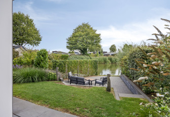 Vista da un lodge al Recreatiepark het Esmeer nei Paesi Bassi con sedie da giardino e canale sullo sfondo.