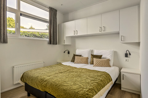 Chambre avec lit double, couvre-lit vert, armoires blanches et grandes fenêtres à Module Special 4 personen.