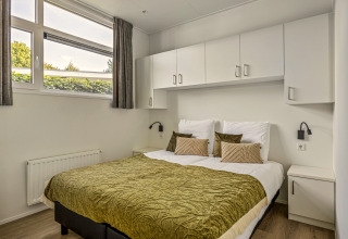 Chambre avec lit double, couvre-lit vert, armoires blanches et grandes fenêtres à Module Special 4 personen.